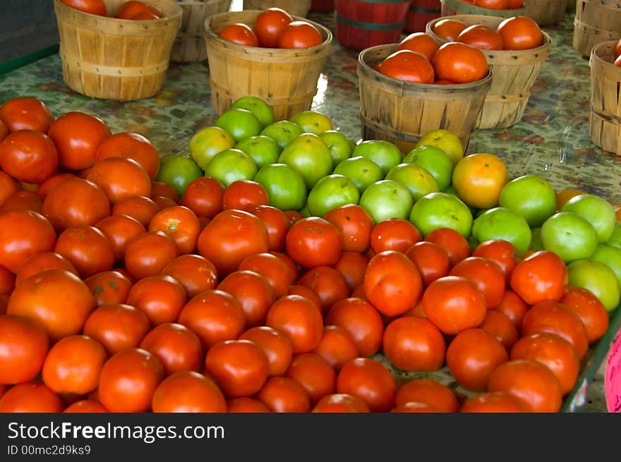 Farmer's market tomato stand with red and green tomatoes and bushel baskets full of tomatoes, fresh produce