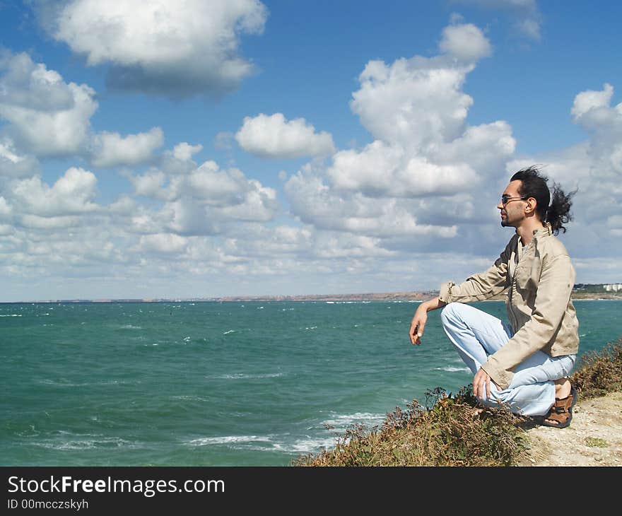 A man over a rock on a blue bay is watching to the horizon. A man over a rock on a blue bay is watching to the horizon