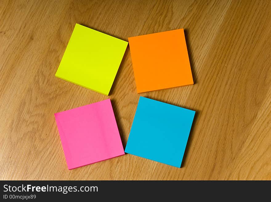 Several blank neon colored post-it notes lying on a wooden floor or desk. Several blank neon colored post-it notes lying on a wooden floor or desk