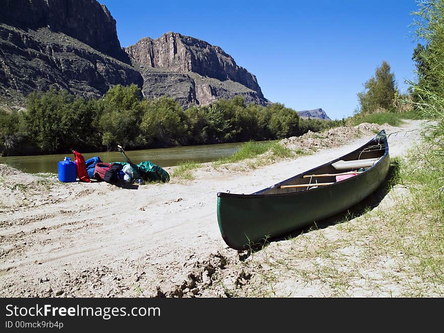 A canoe and gear resting quietly beside a river with majestic cliffs in the background. A canoe and gear resting quietly beside a river with majestic cliffs in the background.