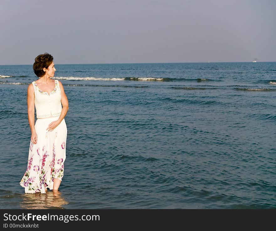 A woman in a long skirt wading in the water along the beach shoreline. A woman in a long skirt wading in the water along the beach shoreline.