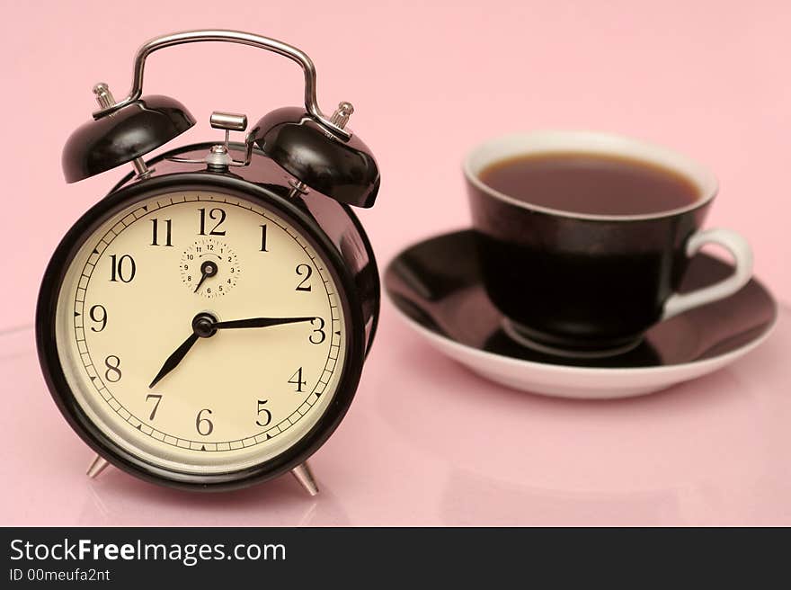 The black alarm clock and black cup from coffee is on a pink background