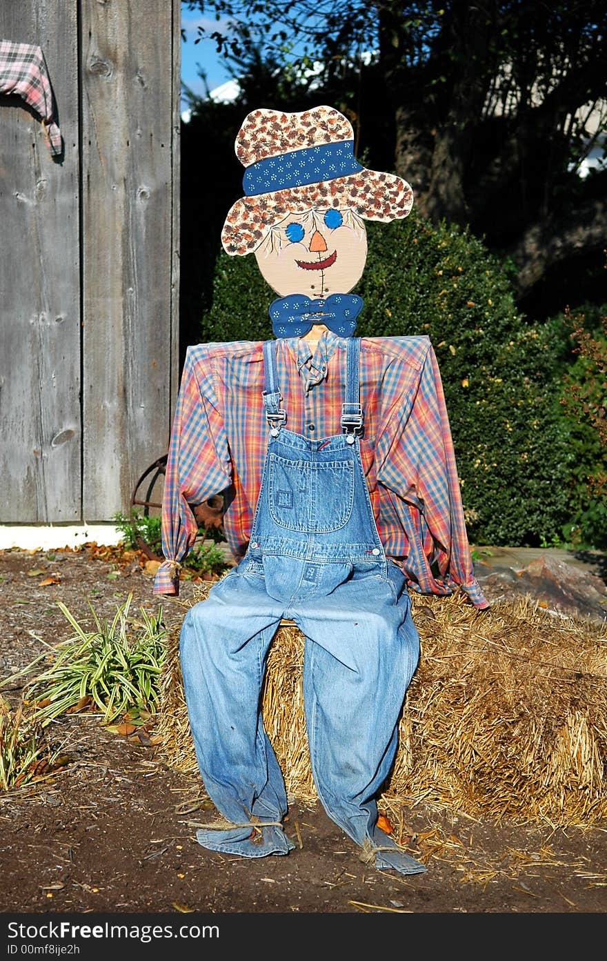 Scarecrow sitting on a bale of hay.