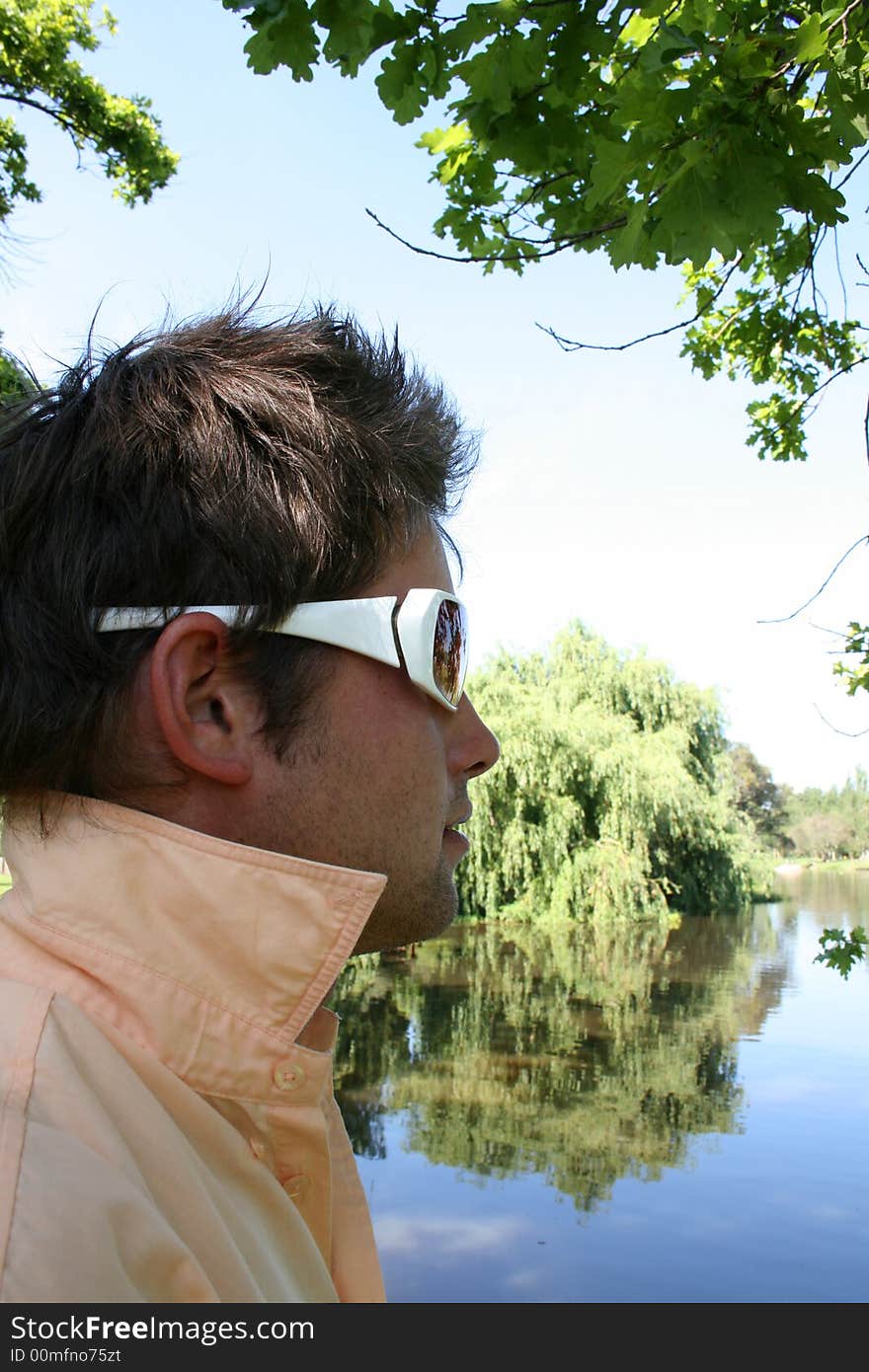 Young male model at the edge of the water, sitting in the shade. Young male model at the edge of the water, sitting in the shade