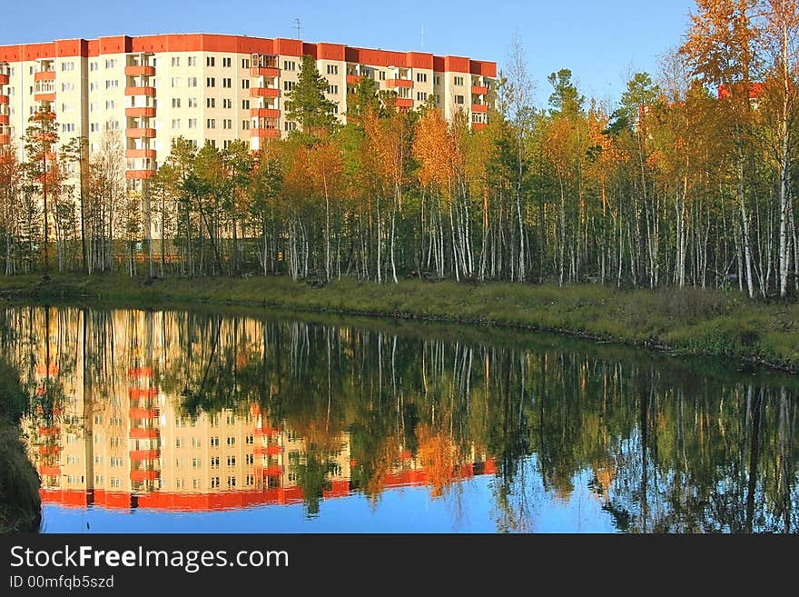 Yellow autumn trees in park on a background of a modern building and a pond