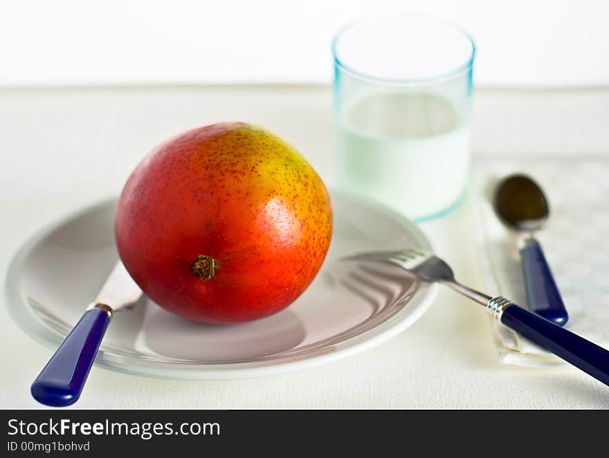 A breakfast table with a juicy and colourful mango fruit ready to be eaten (with shallow DOF). A breakfast table with a juicy and colourful mango fruit ready to be eaten (with shallow DOF).