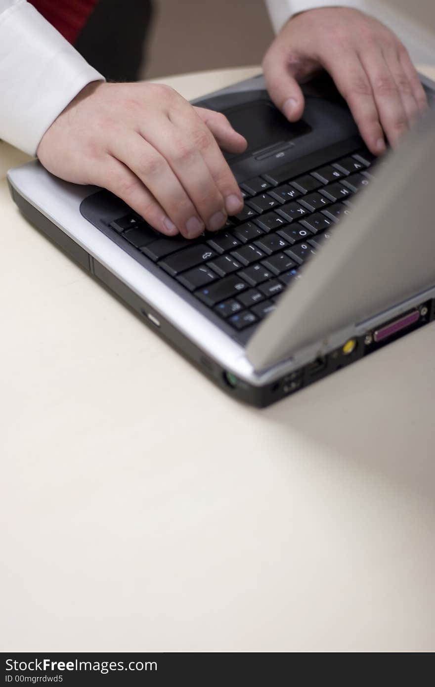 Close up shot of young man's hands typing on keyboard of laptop resting on white table