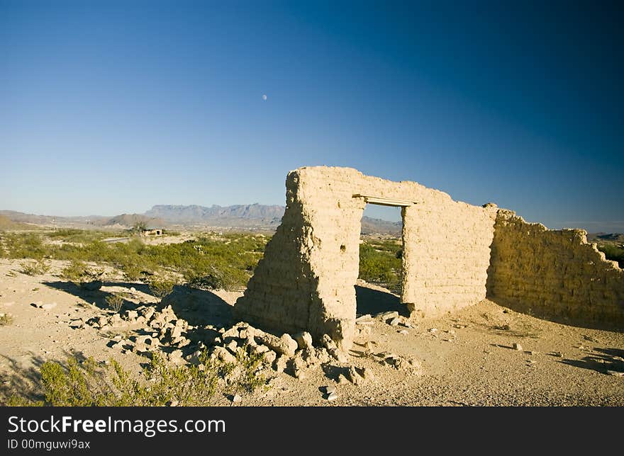 Adobe ruins with mountains and the moon slightly visible in the big blue backdrop of sky. Adobe ruins with mountains and the moon slightly visible in the big blue backdrop of sky.