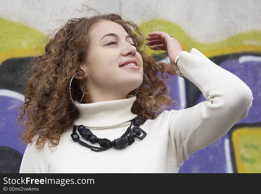 Girl with curling hair near the graffiti wall is smilingto the wind. Girl with curling hair near the graffiti wall is smilingto the wind