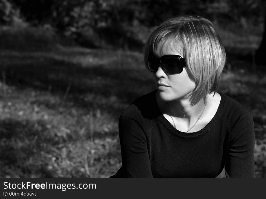 Pretty young woman in sunglasses dreaming sitting in the park