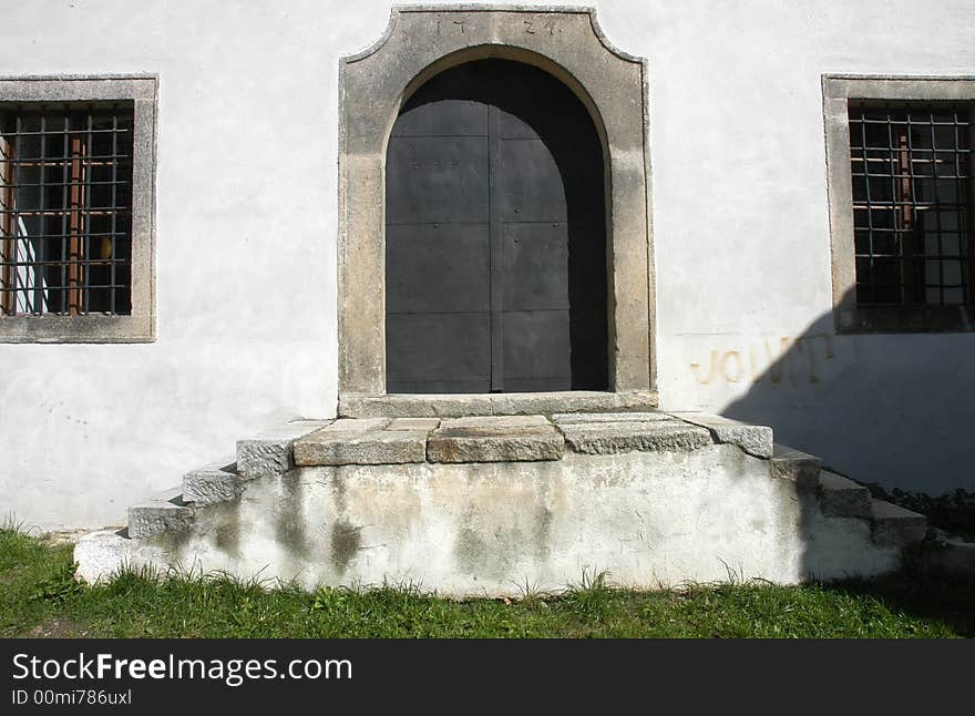 A detail of an old door wit stony stairs leading up to them and two grilled windows