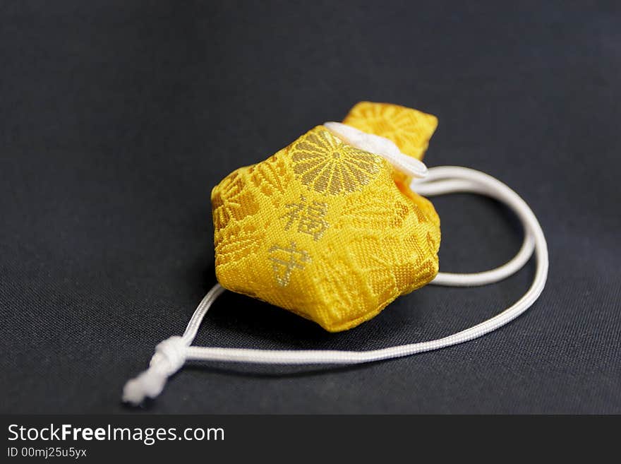 Closeup detail of a yellow asian religious charm on dark black cloth.