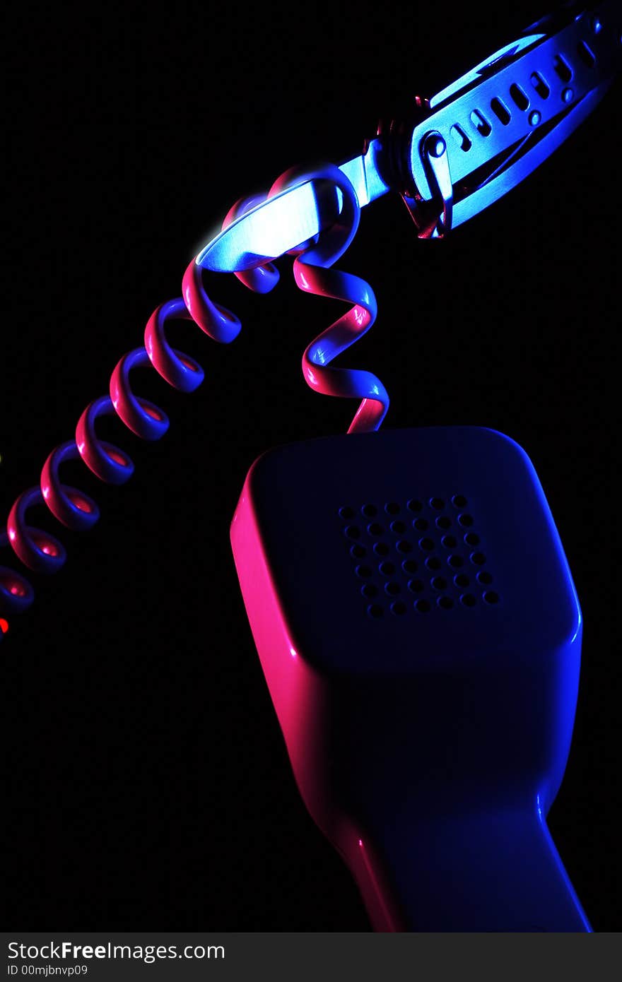 Attempt to cut spiral shaped wire of the telephone handset by swiss knife illuminated by blue and pink colored light sources on the black background. Attempt to cut spiral shaped wire of the telephone handset by swiss knife illuminated by blue and pink colored light sources on the black background