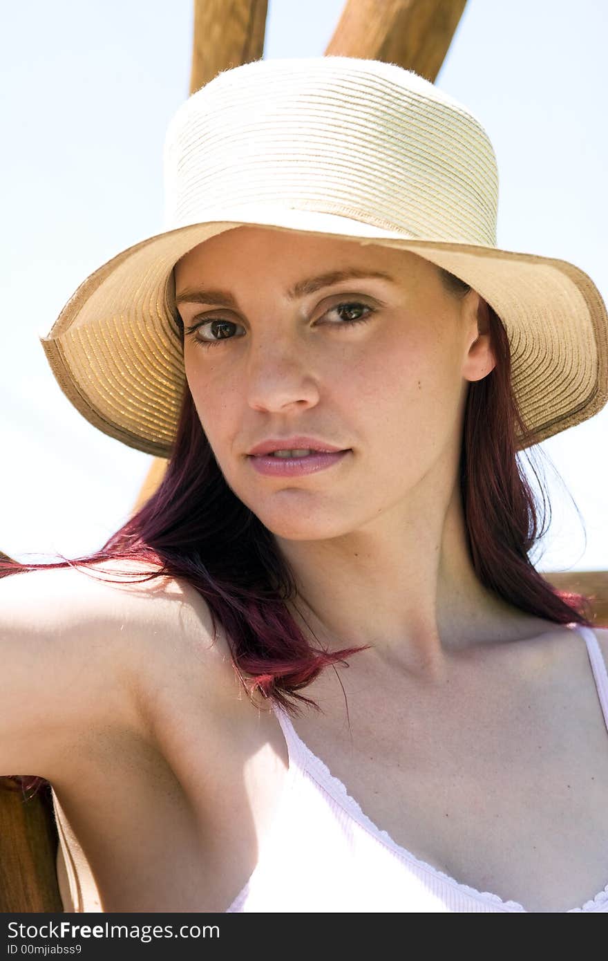 Beautiful woman with a summer hat sitting in the sun on a wooden swing.