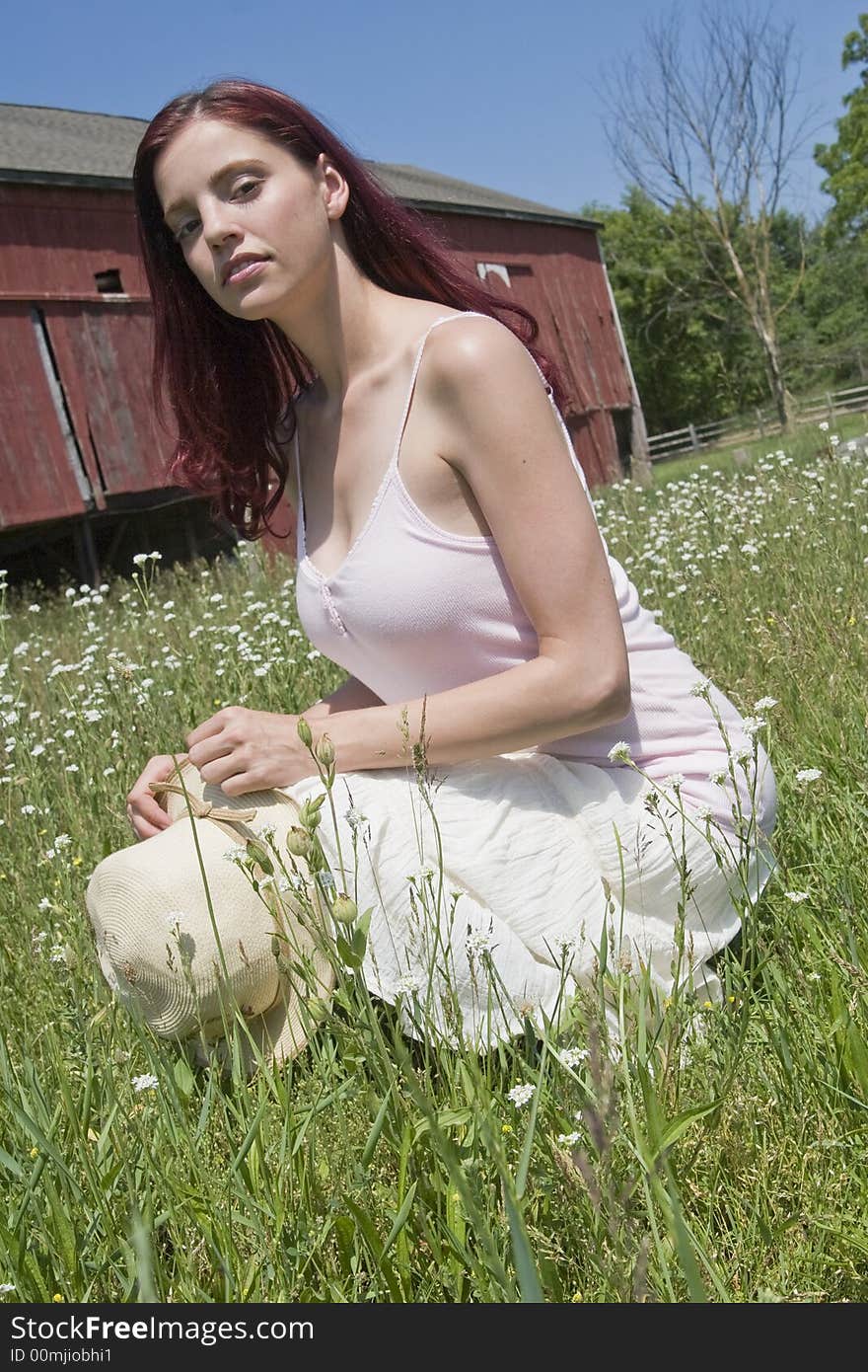 Pretty young woman with a hat posing in a field of wild flowers with a red barn in the background. Pretty young woman with a hat posing in a field of wild flowers with a red barn in the background