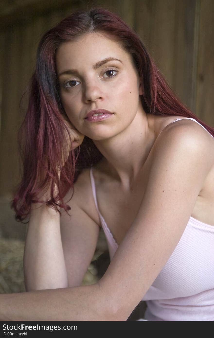 Beautiful young woman sitting in a sunlit barn looking thoughtful. Beautiful young woman sitting in a sunlit barn looking thoughtful.