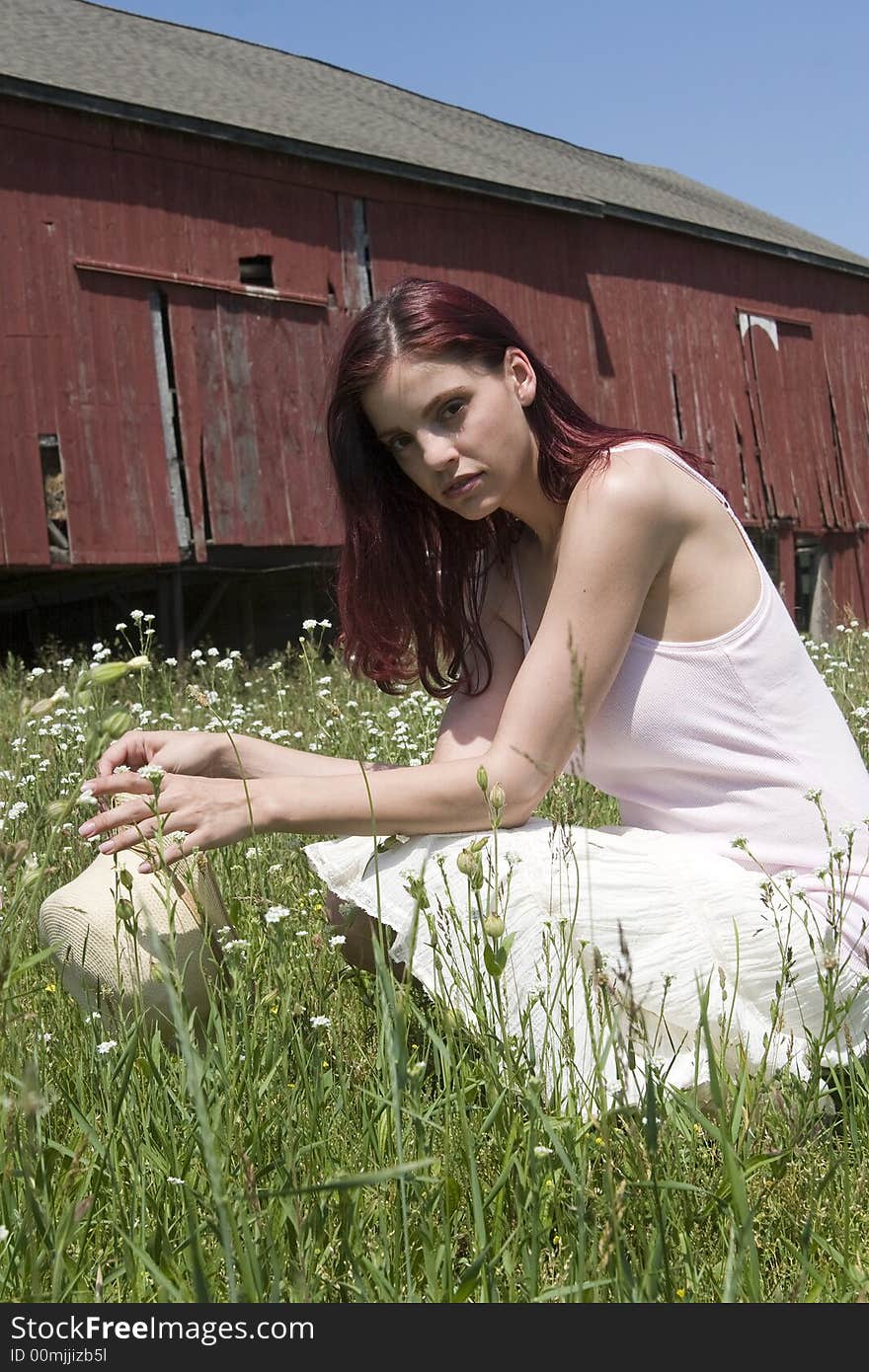 Beautiful young woman kneeling amid a field of wildflowers with an old barn in the background