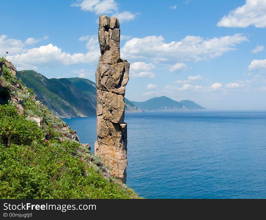 On foreground the single vertical rock with name Hare. On background turquoise sea, cliffs and sky with white clouds. Russian Far Easr, Primorye, Japanese sea, Tasovaya Bay. On foreground the single vertical rock with name Hare. On background turquoise sea, cliffs and sky with white clouds. Russian Far Easr, Primorye, Japanese sea, Tasovaya Bay.