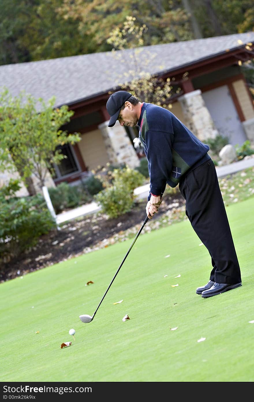 Man teeing off in front of the golf club house on a beautiful fall day. Man teeing off in front of the golf club house on a beautiful fall day.