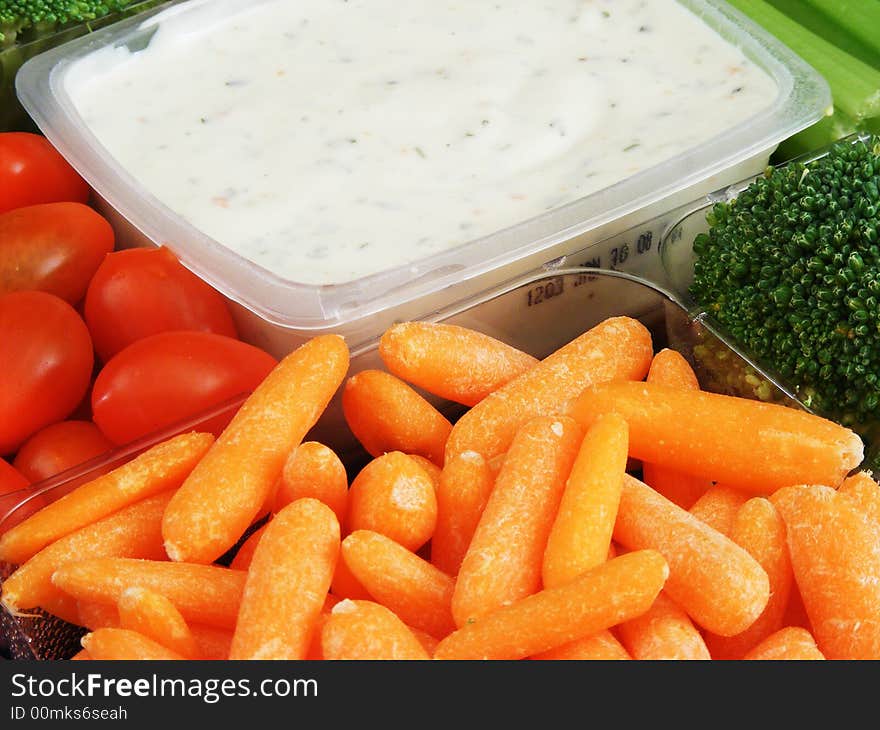 A vegetable tray containing various veggies and dip against a black background. A vegetable tray containing various veggies and dip against a black background.