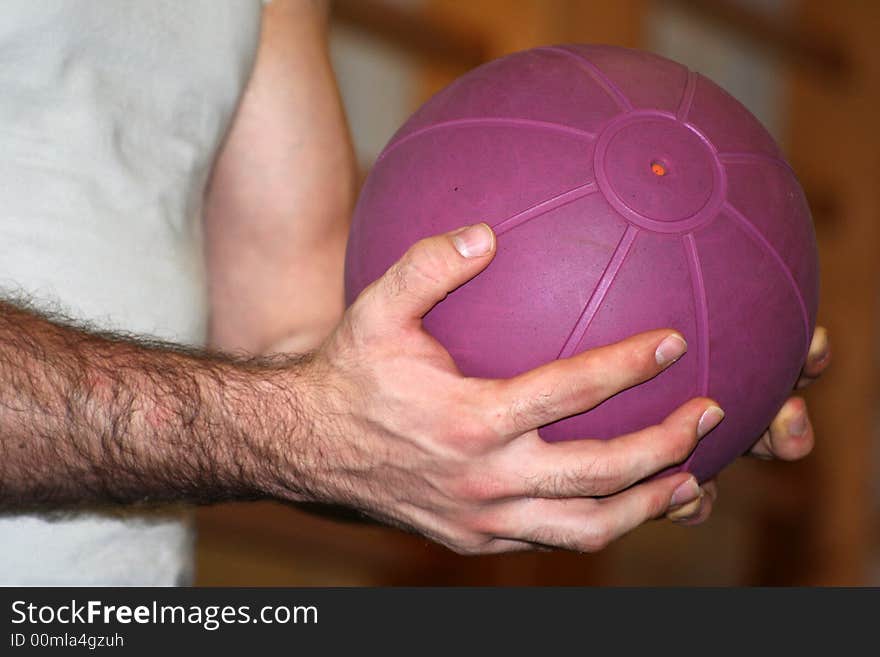 Two hands holding in suspension a purple medical ball for a exercise in the gym / Wall Bars in Blurred Background. Two hands holding in suspension a purple medical ball for a exercise in the gym / Wall Bars in Blurred Background