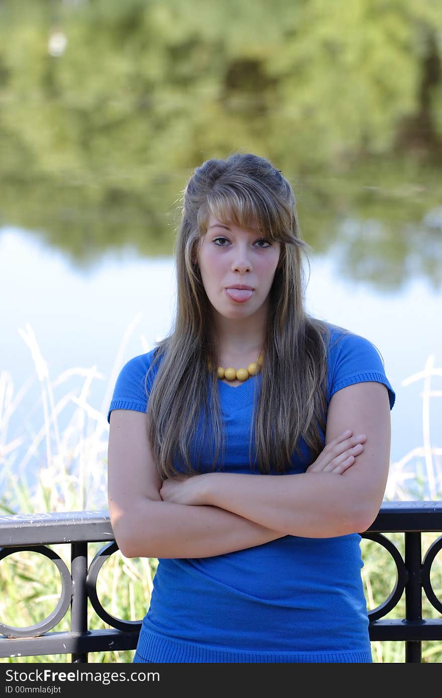 A pretty teenage girl sticking her tongue out while standing against a black cast iron railing near a river front. A pretty teenage girl sticking her tongue out while standing against a black cast iron railing near a river front.