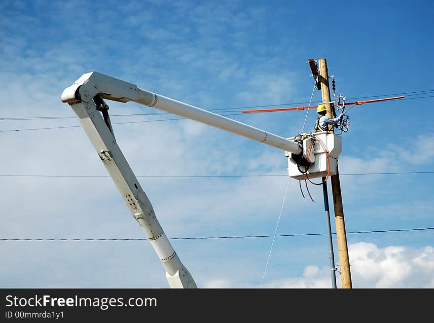 View of man in crane working on powerlines with blue sky in background. View of man in crane working on powerlines with blue sky in background