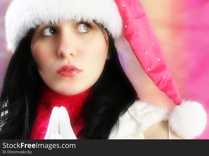 Beautiful young woman making Christmas wish. Wearing pink santa hat and white gloves.