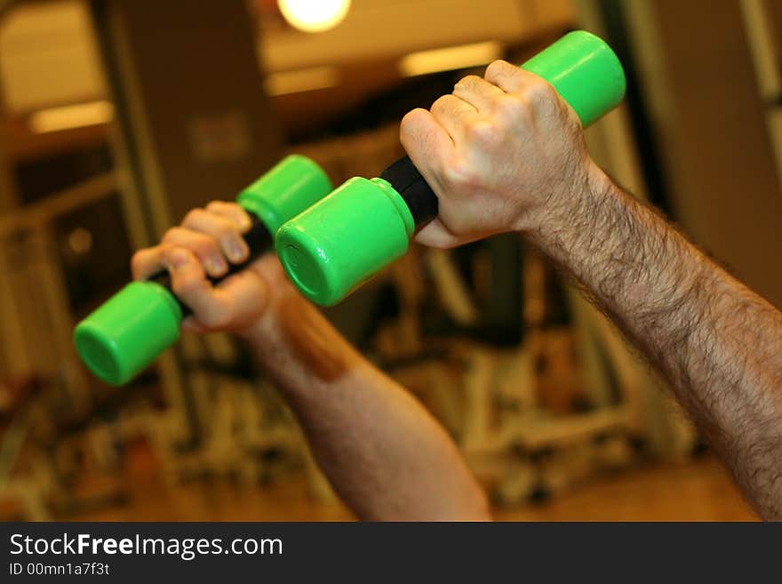 Two hands held close two green Dumbbells / Exercises in the gym / Blur Gym Background. Two hands held close two green Dumbbells / Exercises in the gym / Blur Gym Background