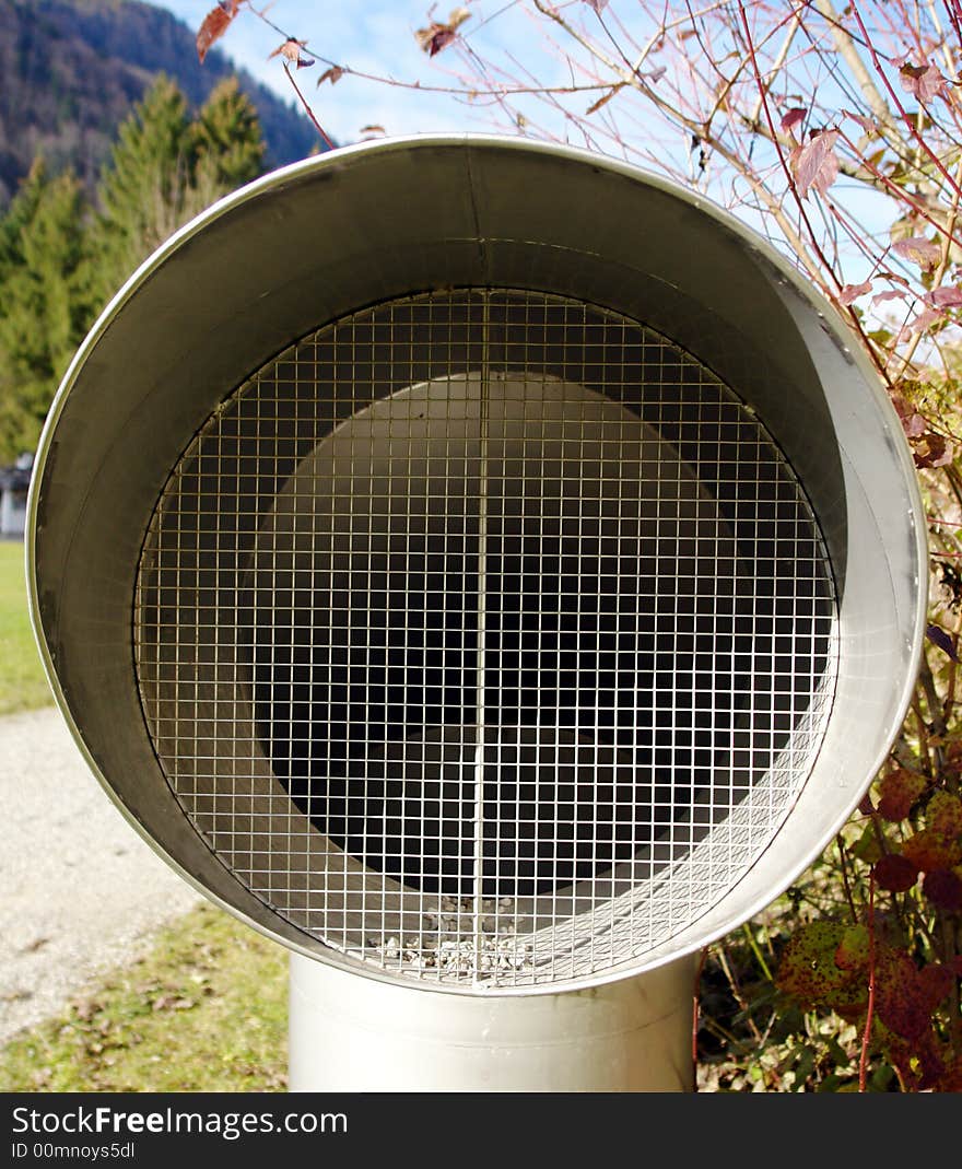 Iron lattice of a big ventilating pipe. Mountain in a distance. Some branches with red leaves as a background. Iron lattice of a big ventilating pipe. Mountain in a distance. Some branches with red leaves as a background.