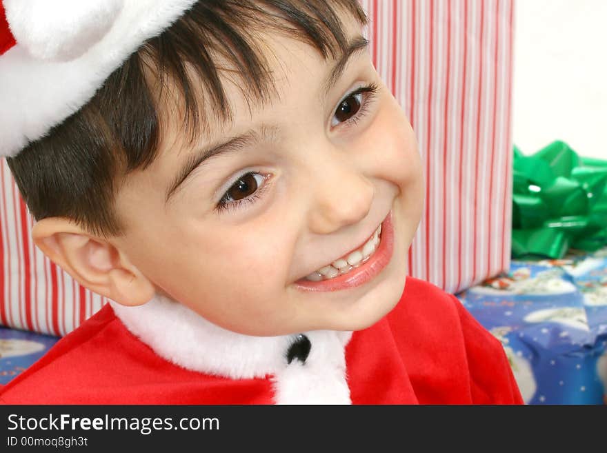 Toddler boy dressed in Santa suit sitting on packages.  Smiling. Toddler boy dressed in Santa suit sitting on packages.  Smiling.