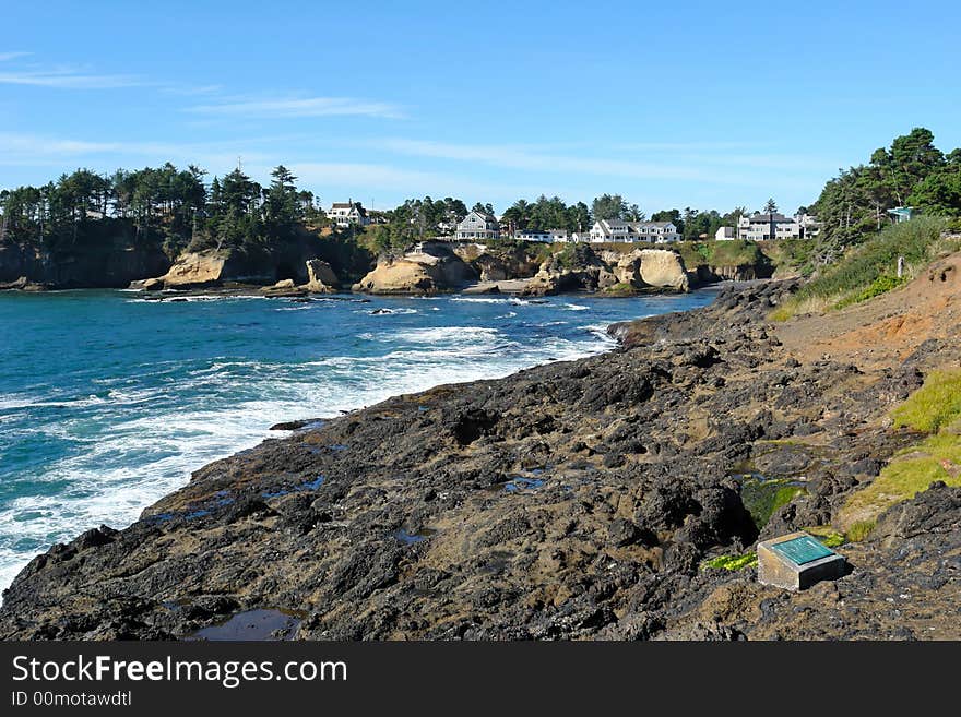 Scenic image of waves crashing on the oregon coast, with seagulls on the ledge and houses in the background. Scenic image of waves crashing on the oregon coast, with seagulls on the ledge and houses in the background