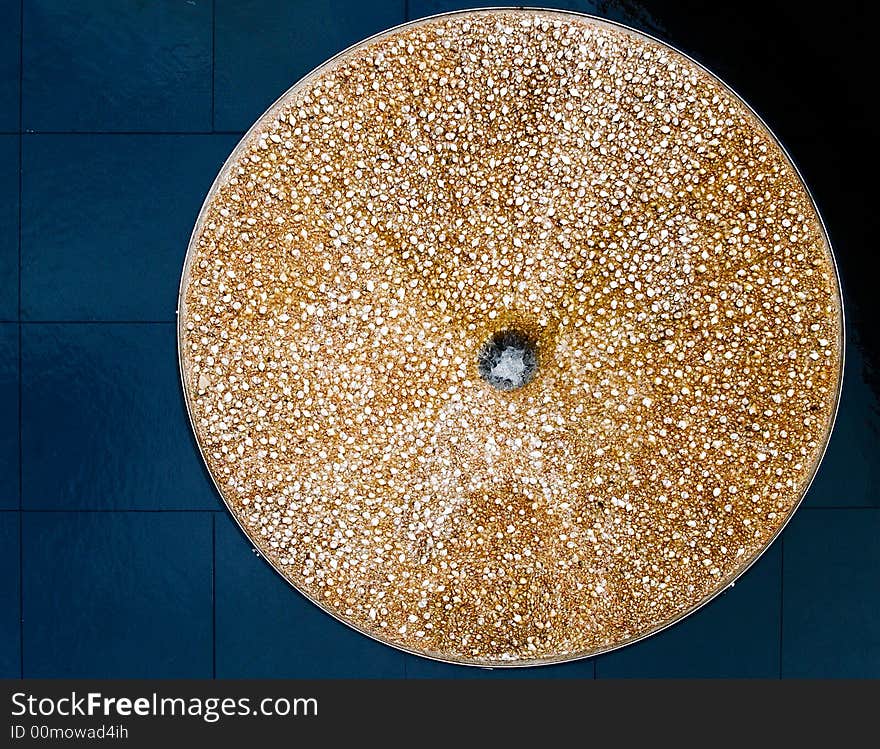 A circular shaped fountain encrusted with seashells on a black marble floor. A circular shaped fountain encrusted with seashells on a black marble floor