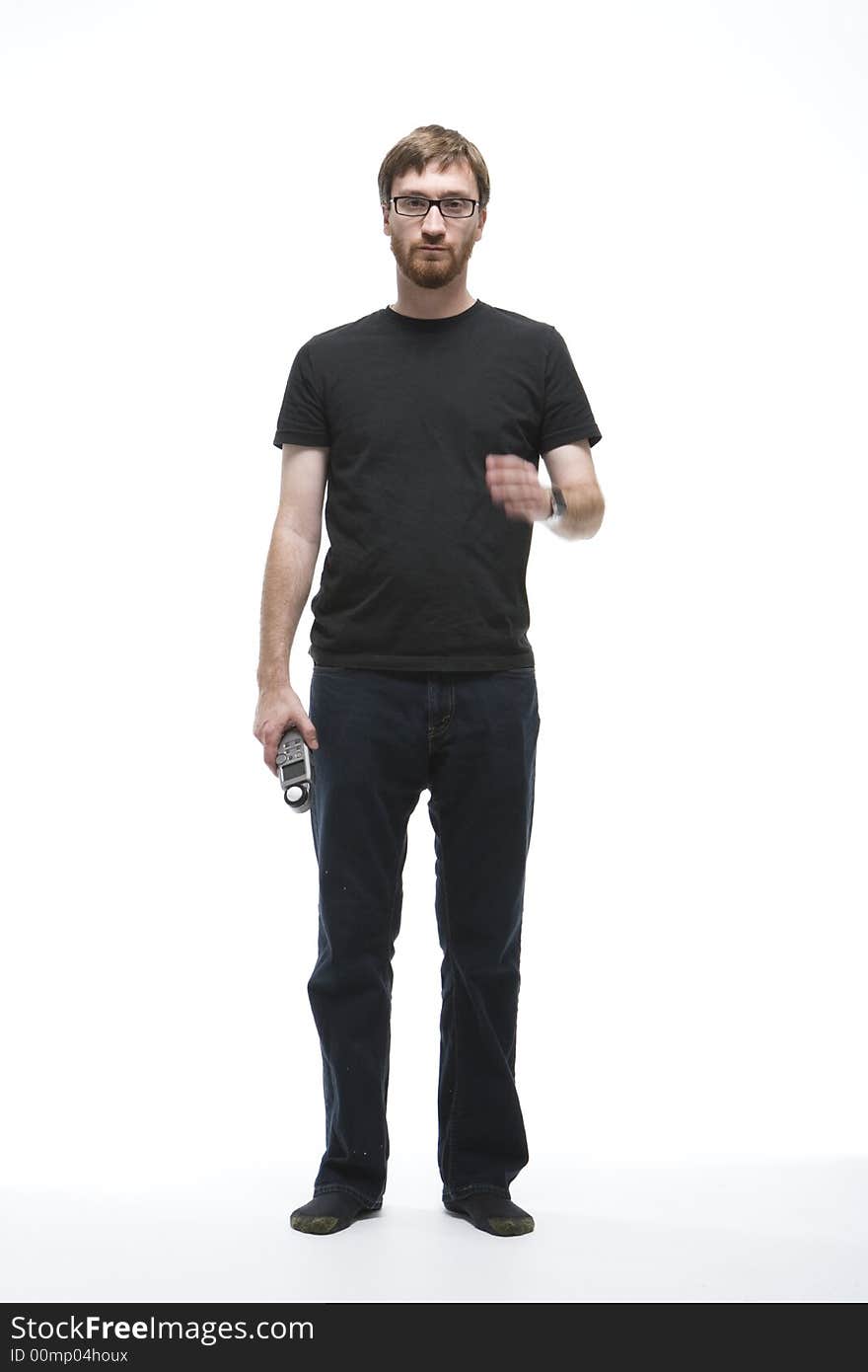 Man with beard wearing a black T-shirt and denim pants stands. He is holding a light meter with one hand and moving the other towards his face. Man with beard wearing a black T-shirt and denim pants stands. He is holding a light meter with one hand and moving the other towards his face.