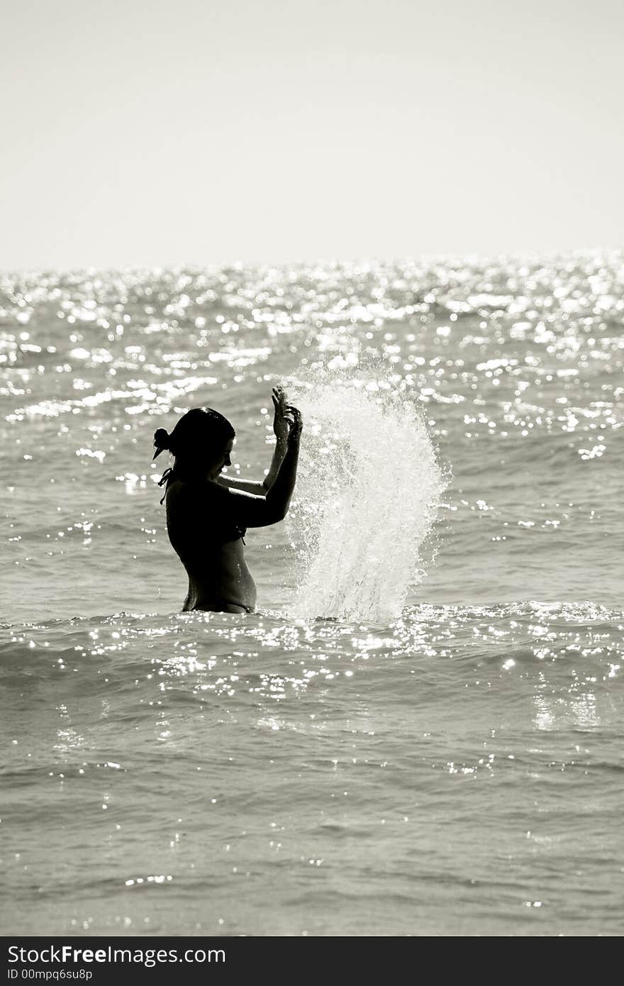 Silhouette of a wet young woman in a waving sea splashing the water, vertical. Silhouette of a wet young woman in a waving sea splashing the water, vertical