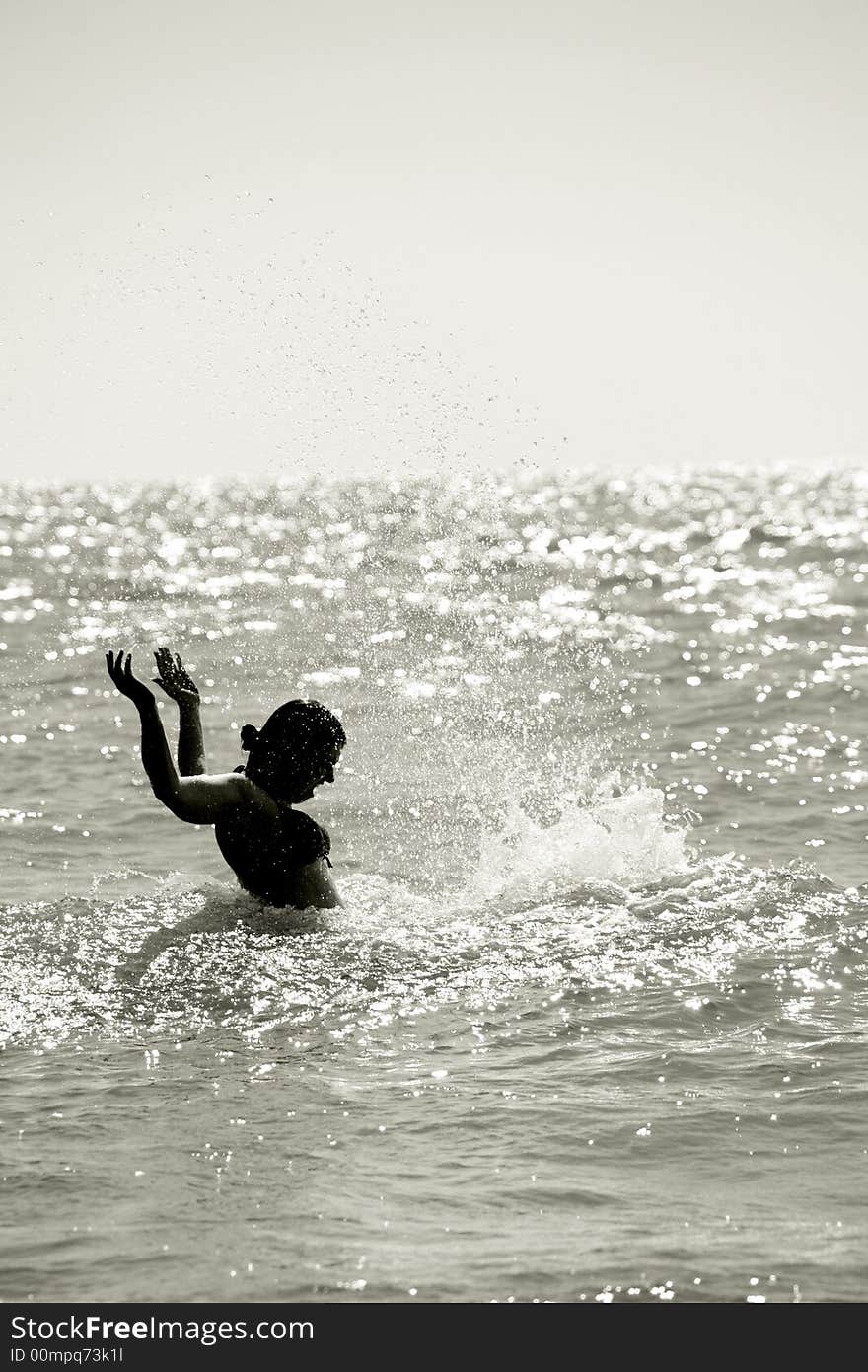 Silhouette of a wet young woman in a waving sea splashing the water, vertical. Silhouette of a wet young woman in a waving sea splashing the water, vertical