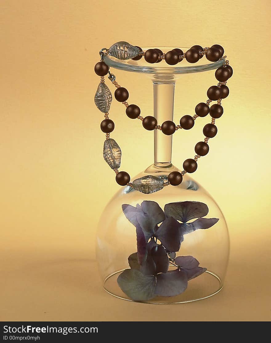 Still life with a braceles, a dry flower and one wineglass on orange background. Still life with a braceles, a dry flower and one wineglass on orange background