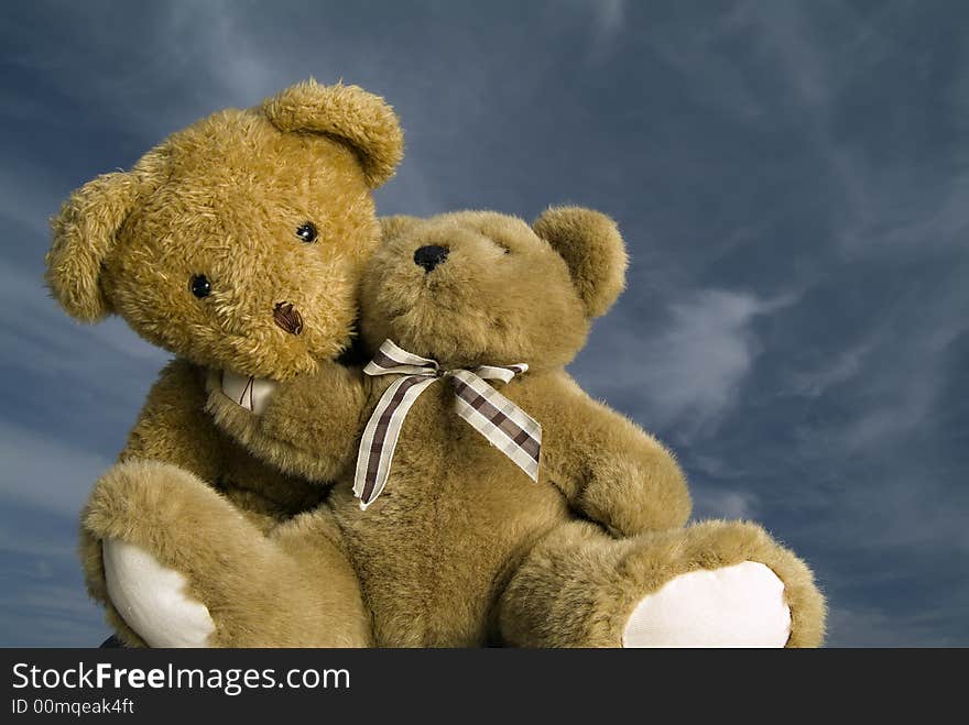 Two teddy bears hugging each other agaist blue sky with cirrus clouds. Two teddy bears hugging each other agaist blue sky with cirrus clouds