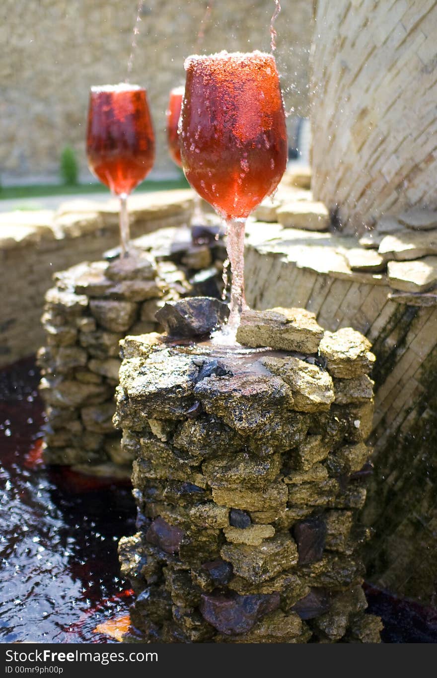 Fountain with red wine pouring into huge glasses on stones. Fountain with red wine pouring into huge glasses on stones.