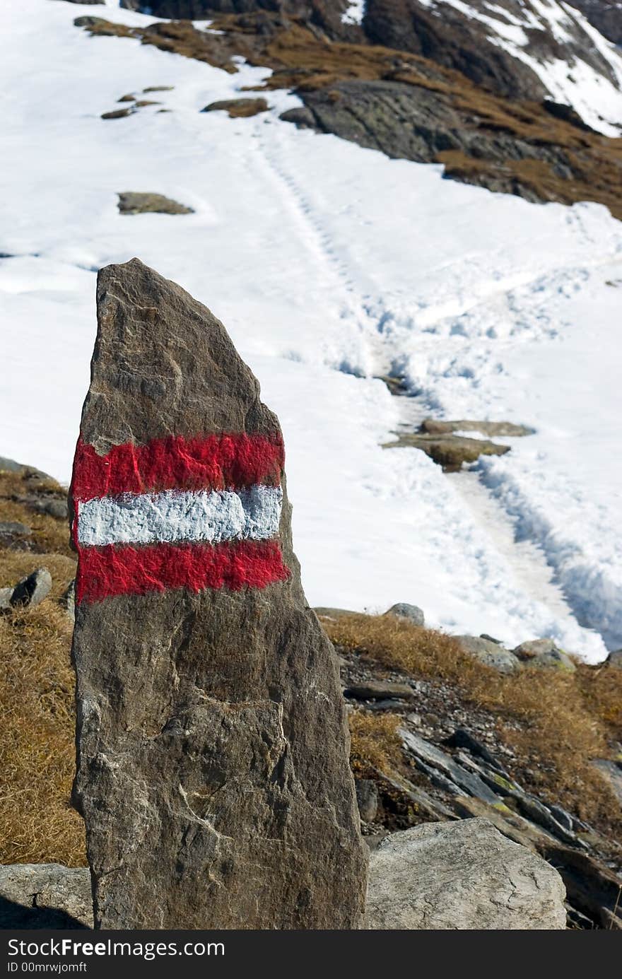 Red marking on stone, in background footpath in snow, Alps