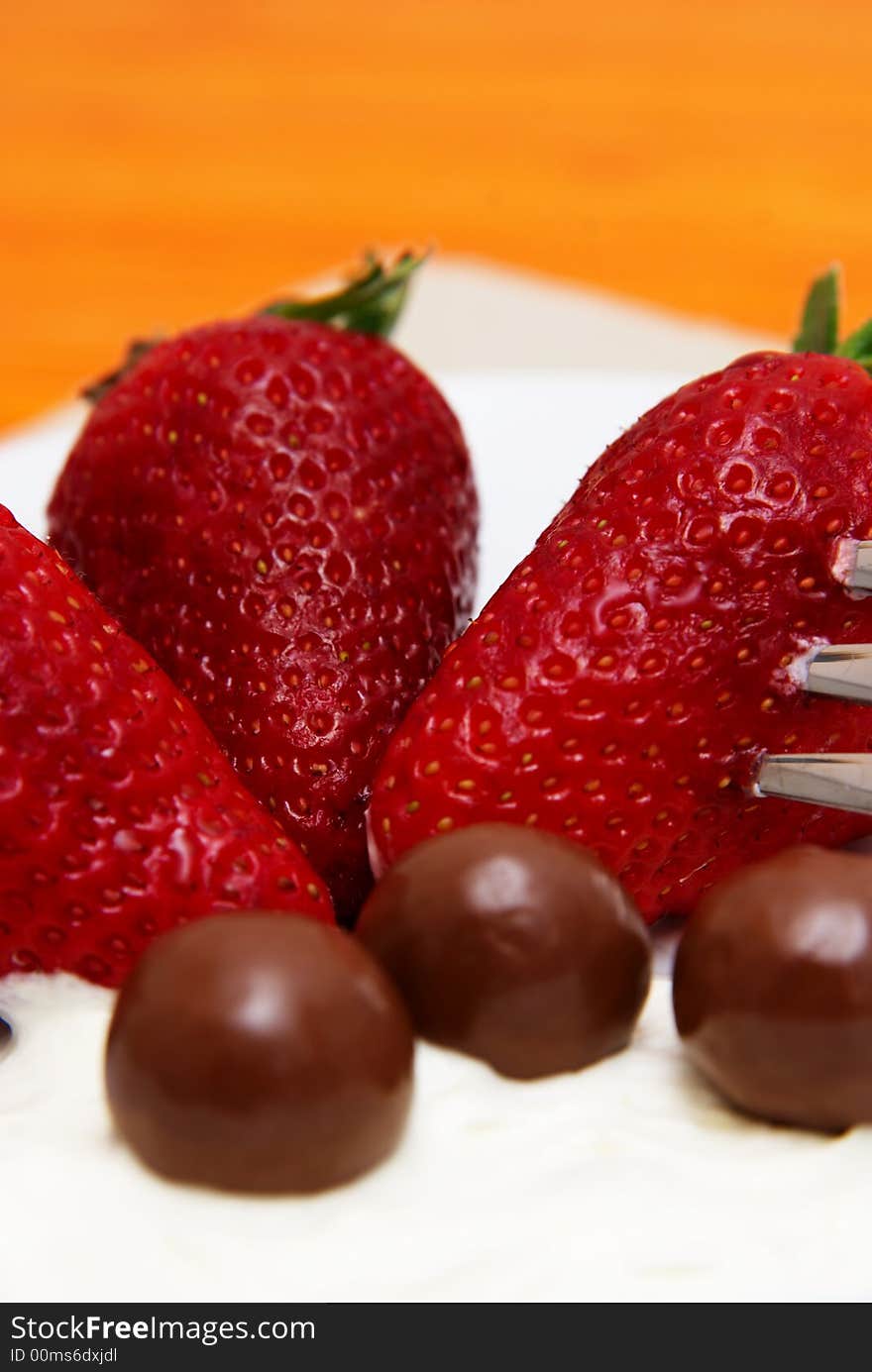 Three strawberries with chocolate balls lying in cream on white saucer. Three strawberries with chocolate balls lying in cream on white saucer
