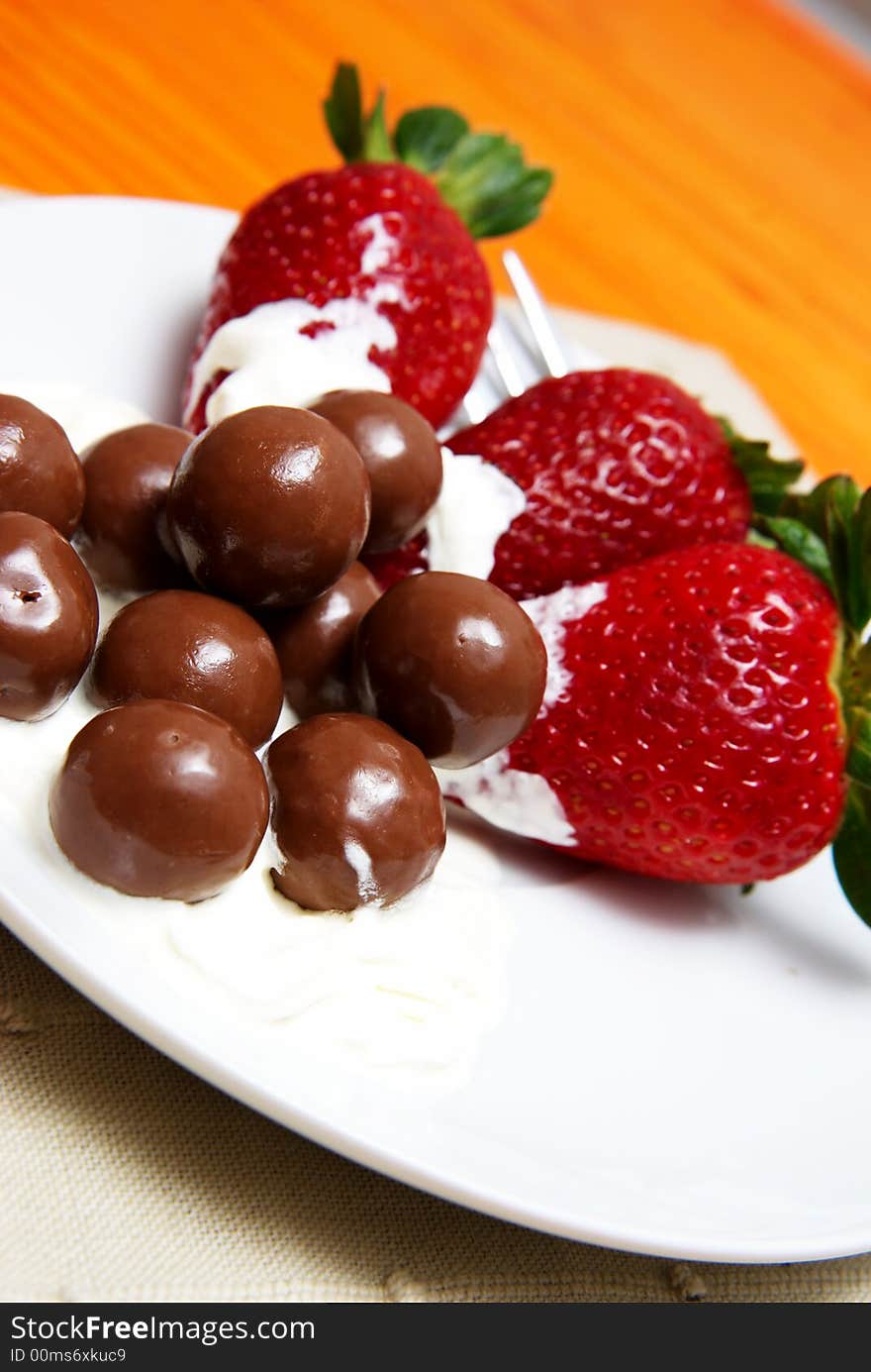 Three strawberries with chocolate balls lying in cream on white saucer. Three strawberries with chocolate balls lying in cream on white saucer