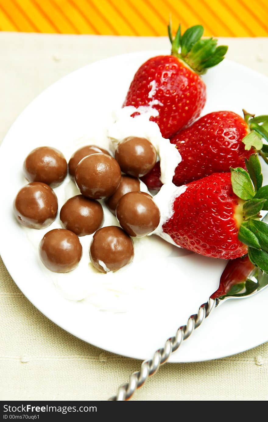 Three strawberries with chocolate balls lying in cream on white saucer. Three strawberries with chocolate balls lying in cream on white saucer