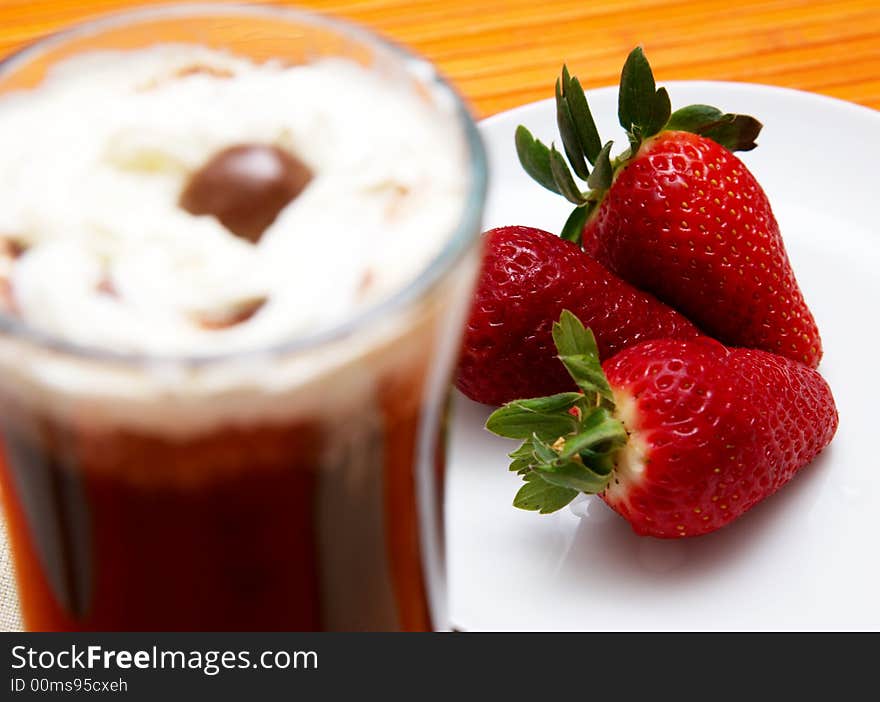 Cup of coffee with cream and three strawberries on a saucer. Focus is on the strawberries. Cup of coffee with cream and three strawberries on a saucer. Focus is on the strawberries