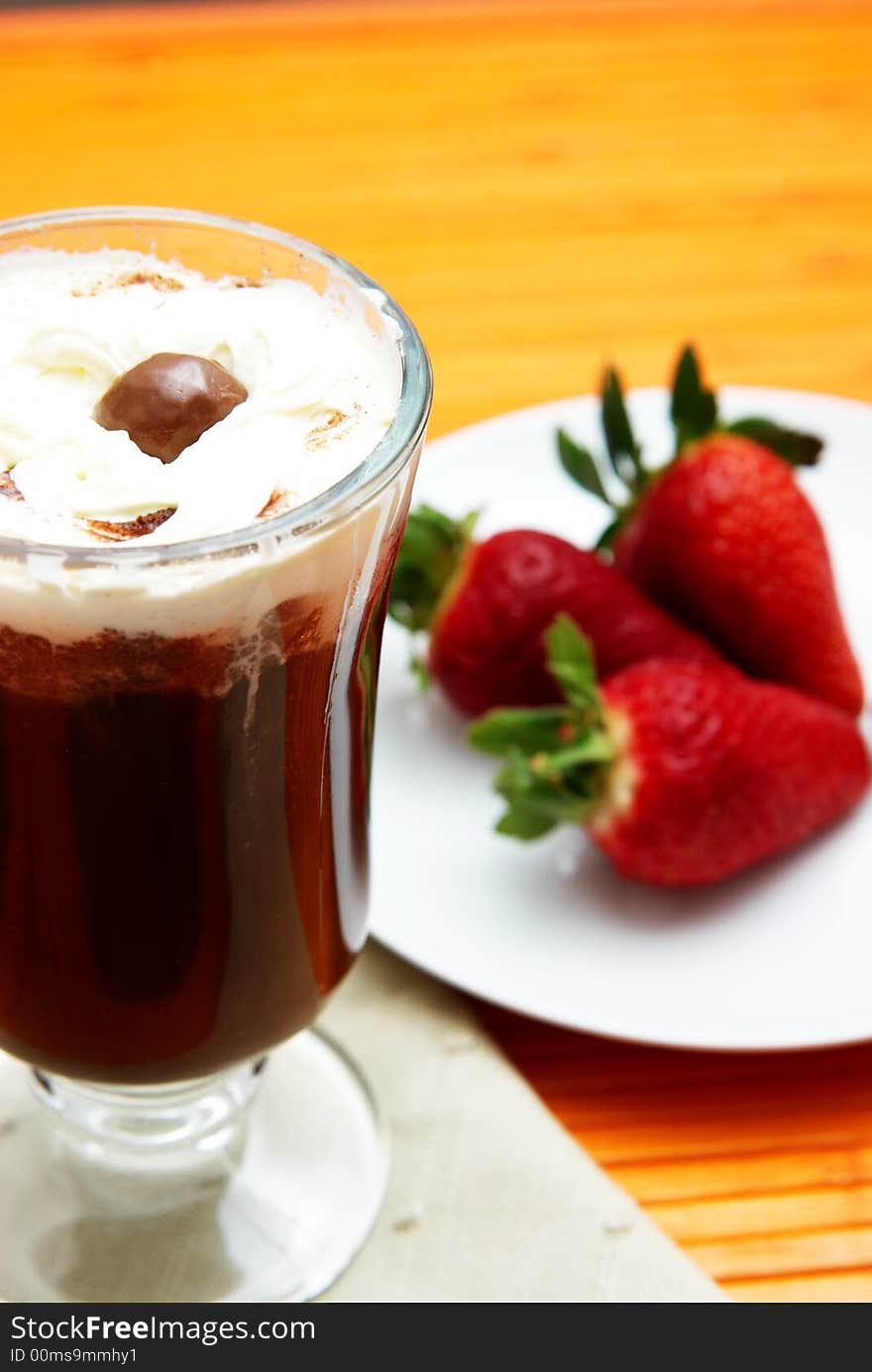 Cup of coffee with cream and three strawberries on a saucer. Focus is on the chocolate ball in the coffee. Cup of coffee with cream and three strawberries on a saucer. Focus is on the chocolate ball in the coffee