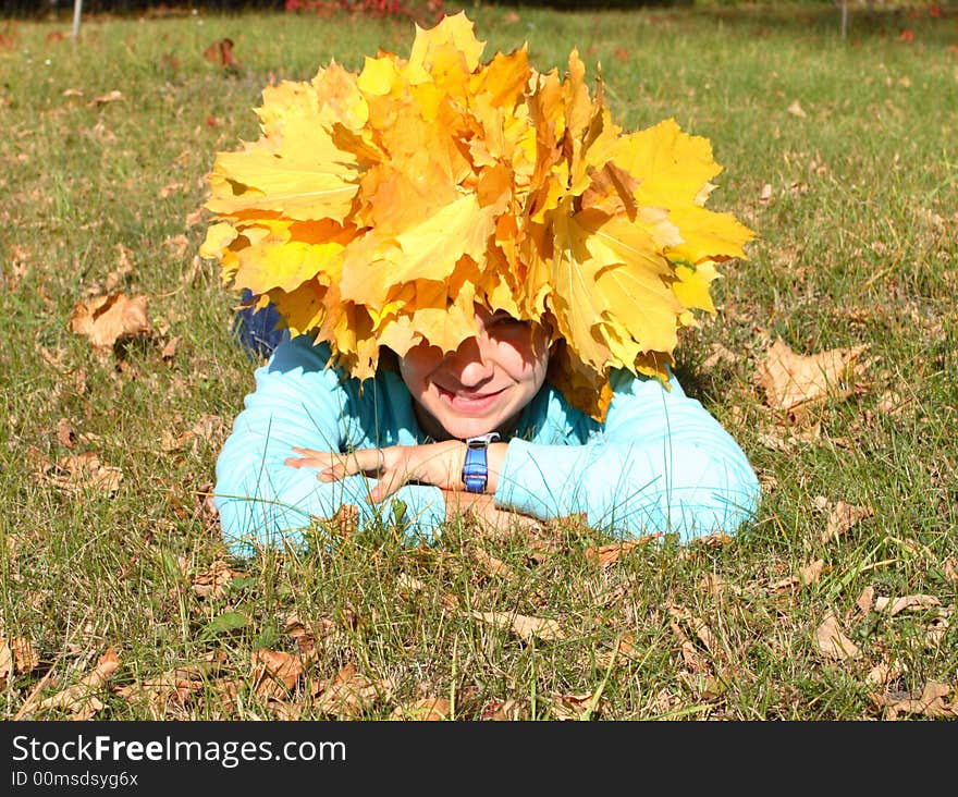 Portrait of the girl in a chaplet from yellow maple leaves lies in a grass