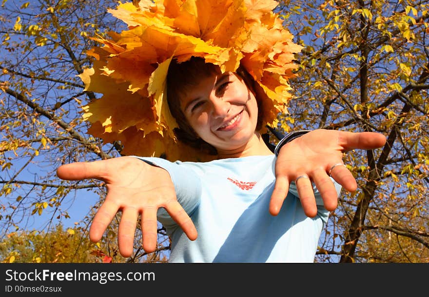 A girl in a chaplet from yellow maple leaves gives hands