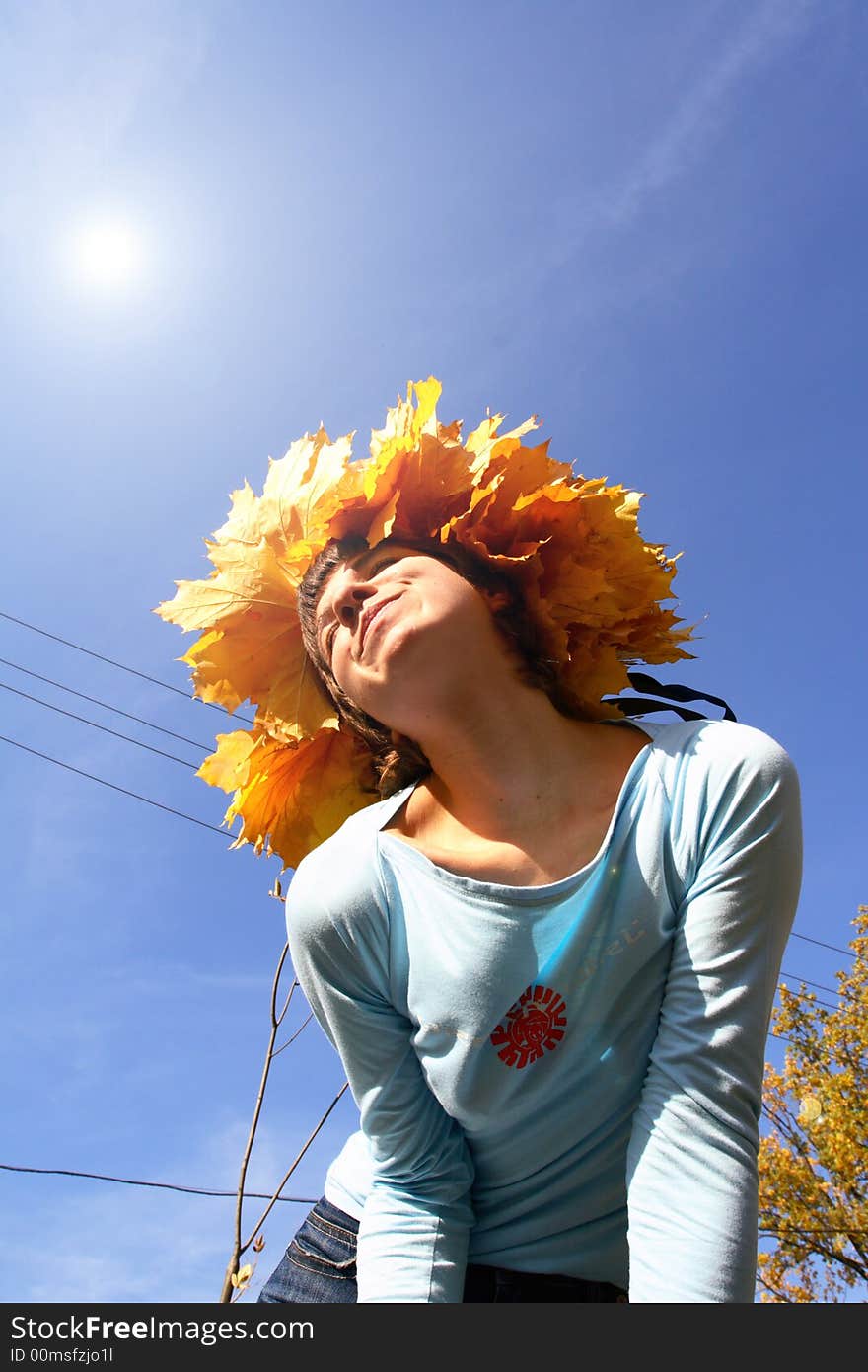 A girl in a chaplet from yellow maple leaves puts a person a sun