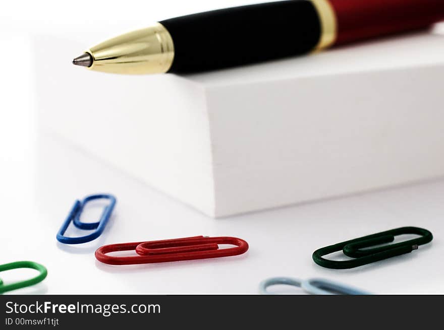 Pen on top of post-it cube with colored paper clips isolated on white. Pen on top of post-it cube with colored paper clips isolated on white