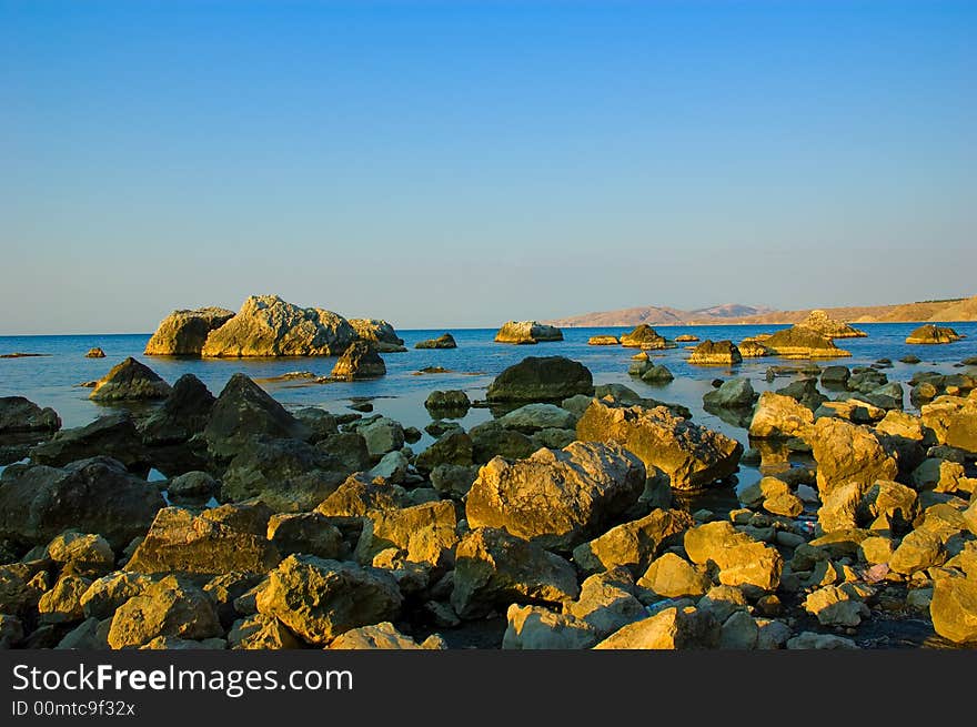 Stones on rays of sunrise. Wild sea coast